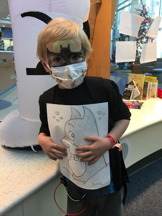 You can't see it, but there's a huge happy grin behind the mask of this young Batman fan who just got an original drawing from a Drawn To Help volunteer.
